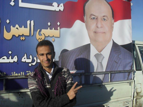 صورة الصحفي معاذ راجح أمام لوحة لحملة انتخاب الرئيس هادي 2012